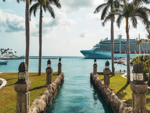 A cruise ship anchored beyond a palm-lined canal in the Caribbean