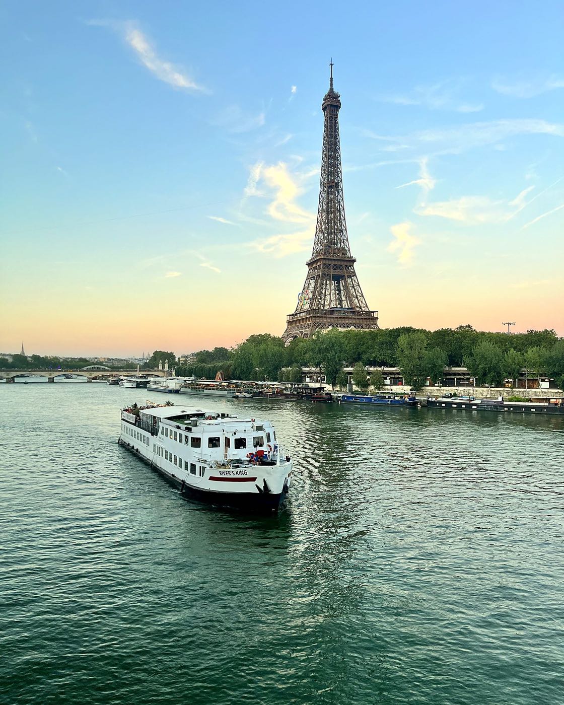 The Eiffel Tower at sunset above the Seine, with a river cruise boat in the foreground