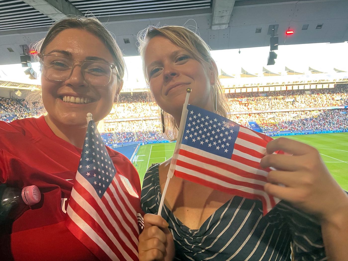 Emily and a friend waving small American flags in the stands at the Parc des Princes
