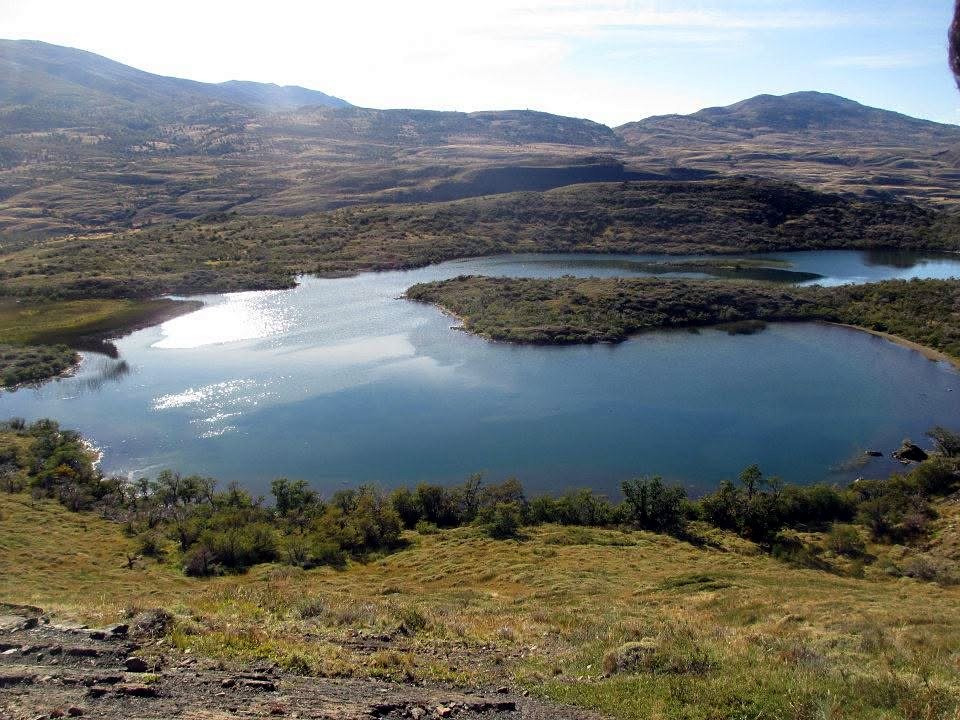 Blue lakes and green islands among golden Patagonian hills under a clear sky