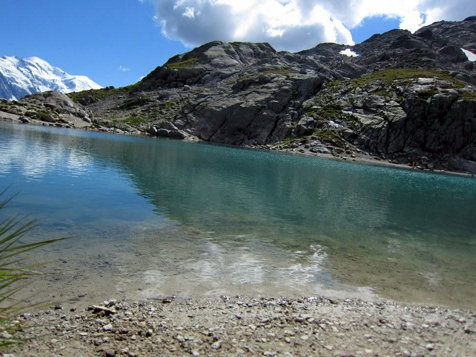 A clear turquoise alpine lake below gray granite and a snowy summit on the Tour du Mont Blanc