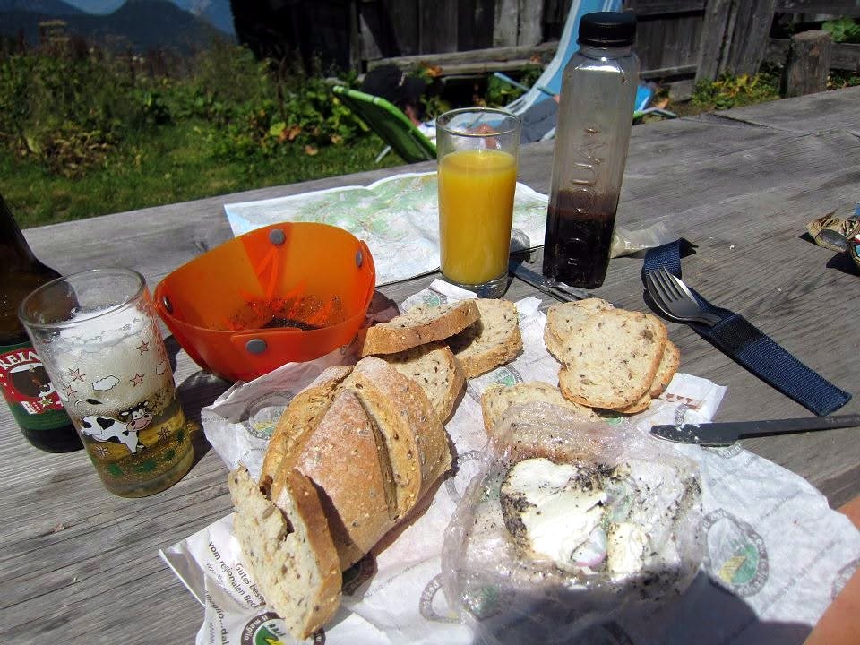 A picnic table with bread, cheese, juice and a trail map in the Alps